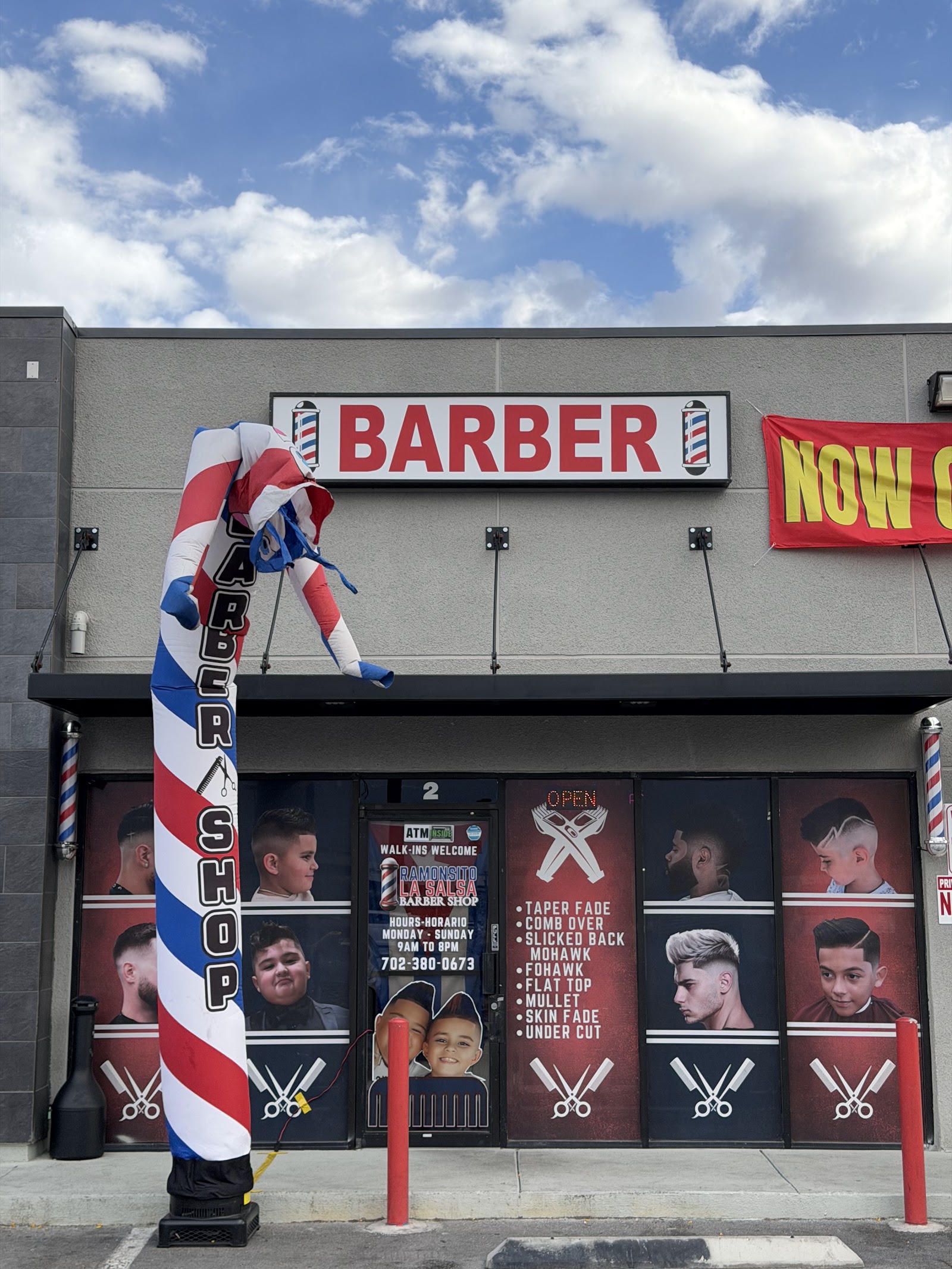 Exterior of Ramonsito La Salsa Barber Shop with BARBER sign, an inflatable barber pole, and window graphics of haircut styles