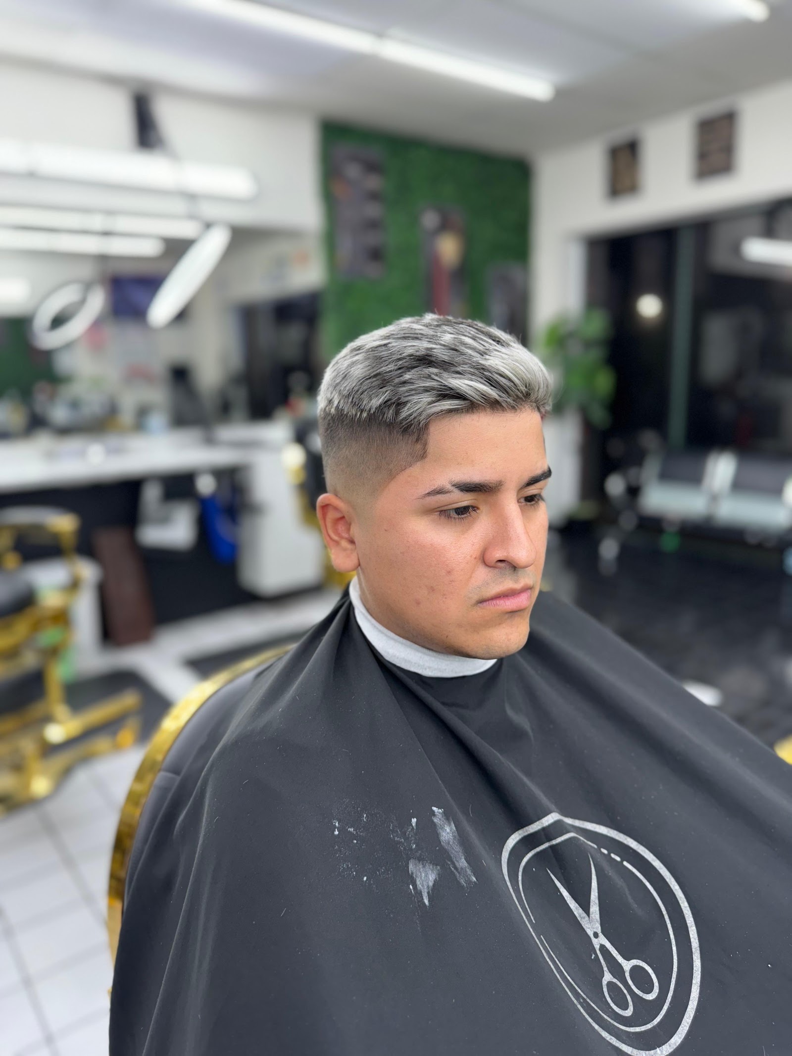 Man with a silver-dyed textured quiff and skin fade wearing a barber cape