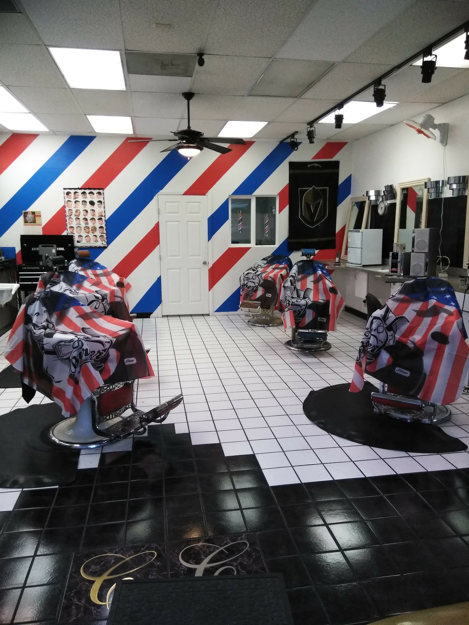 Interior of the barbershop with red white and blue striped walls, barber chairs draped with American flag capes, and a checkered floor