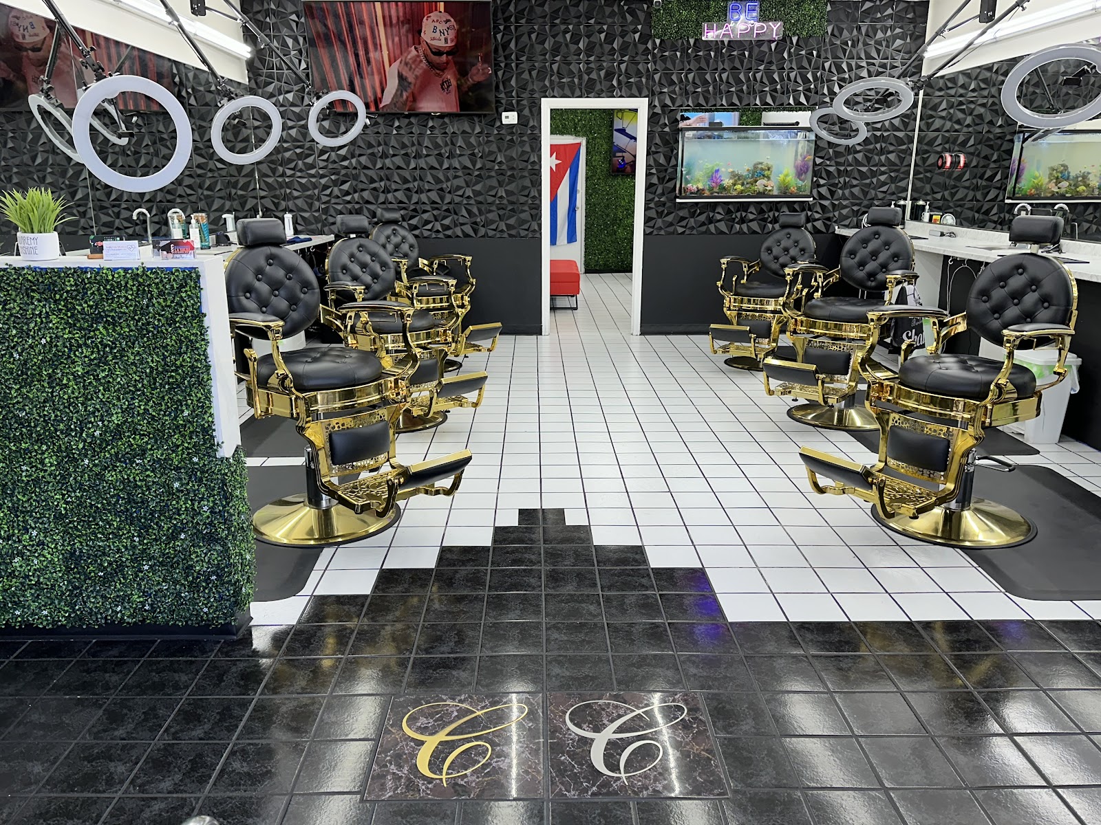 Modern barbershop interior with gold and black barber chairs, textured black walls, a fish tank, and a Cuban flag